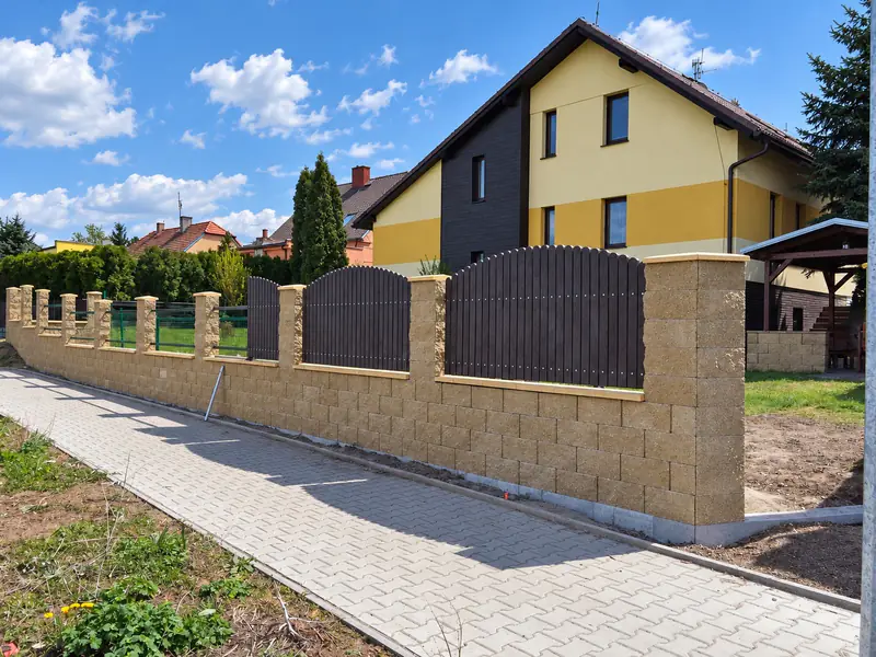 Plot z betonových tvárnic s dřevěnými výplněmi u rodinného domu a chodník ze zámkové dlažby
