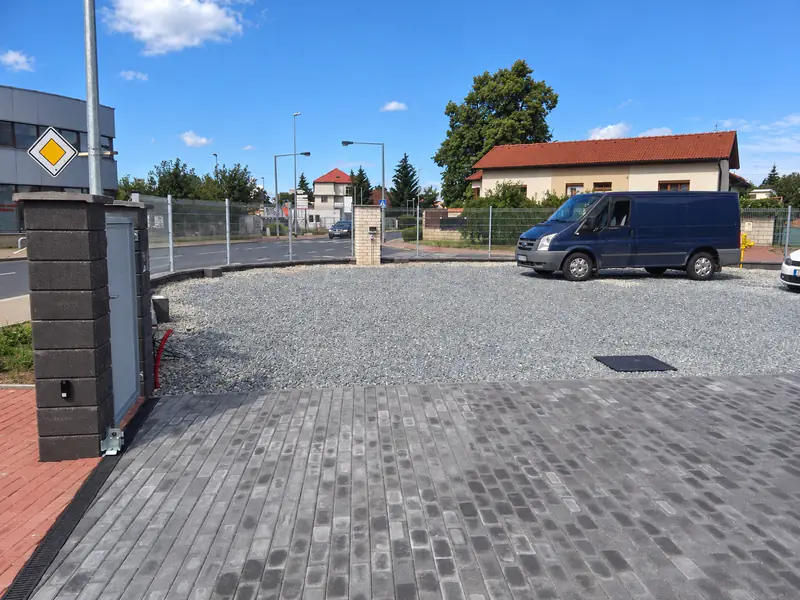 Vjezd z betonové dlažby a zpevněná štěrková plocha u firemního areálu