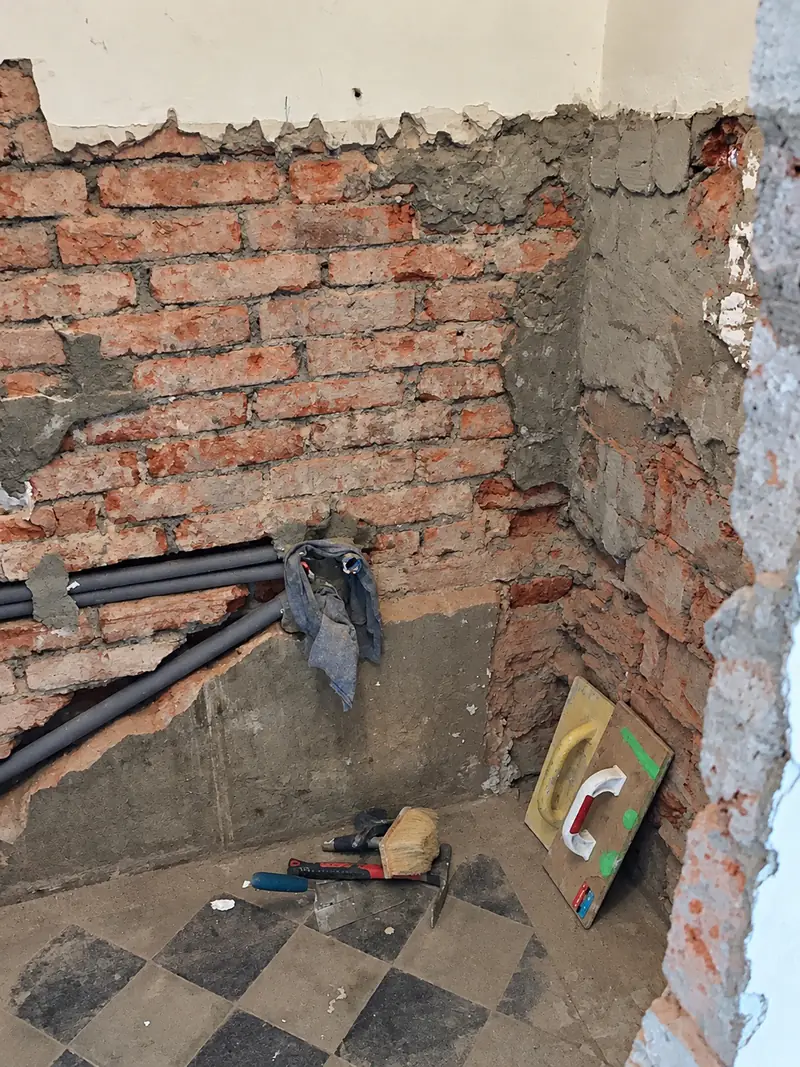 Koupelna po vybourání starého obkladu s odhaleným cihlovým zdivem a rozvody